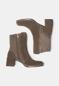 Braune Wildleder-Stiefeletten mit Blockabsatz, seitlichem Reißverschluss und dezenten Nähdetails. Glatte Textur, modernes Design mit einer figurbetonten Silhouette.