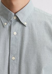 Lichtblauwe geruite overhemd met een button-down kraag. De stof heeft een subtiele textuur, met witte plastic knopen langs de sluiting.
