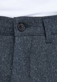 Pantaloni in denim scuro con finitura testurizzata, chiusura con bottoni e passanti per cintura. Il tessuto presenta un leggero motivo a macchie.