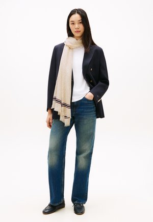 Blazer azul marino, camiseta blanca, pañuelo beige con estampado de rayas rojas, vaqueros azules de pierna recta y zapatos negros. Look limpio y moderno.