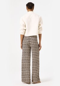 Witte textuur geassembleerde cropped jasje gecombineerd met wijde broek met een geometrisch zwart-wit patroon. Minimalistisch ontwerp met zichtbare naden.