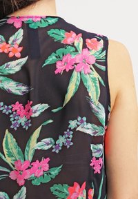 Blusa sin mangas negra con vibrantes patrones florales en rosa, verde y azul sobre una tela transparente, con un escote redondeado.