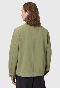 Olivengrønn, oversized jakke med en ren struktur, lange ermer og knappede mansjetter. Har en subtil teksturert stoff og detaljert bakseam.