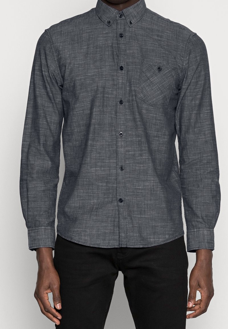 Donkergrijs overhemd met knoopsluiting van een gestructureerde stof, lange mouwen en een enkele borstzak. Zwarte knopen contrasteren met de kleur van het shirt.