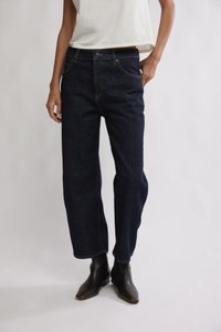 Jean en denim bleu foncé avec une coupe droite, coutures jaunes, fermeture par bouton et poches avant, associé à des bottines noires.