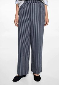 Široké kalhoty v námořnické modři s vertikálními bílými pruhy. Vyrobené z lehkého materiálu, s vysokým pasem a bočními kapsami.