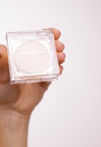 Revolution makeup highlighter i klar plastikkasse, rund panne, myk hvit farge, med preget merkenavn og "BEAM BRIGHT" etikett.