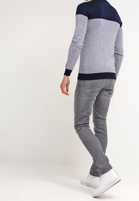 Grauer und marineblauer Pullover mit farbblockiertem Design und enger Passform, kombiniert mit schlanken grauen Jeans und weißen Schuhen. Gestrickte Struktur mit gerippten Bündchen.