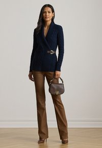 Μπλε ναυτικού καλωδιωτό ζακέτα με χρυσή αγκράφα, συνδυασμένη με καφέ καμπάνα παντελόνια και μία μικρή καφέ τσάντα. Λείο υλικό, εφαρμοστή σχεδίαση.