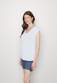 Top azul claro de mangas curtas com decote em V profundo e bainha curva, combinado com uma saia mini de ganga com bordas desfiadas. Textura suave.