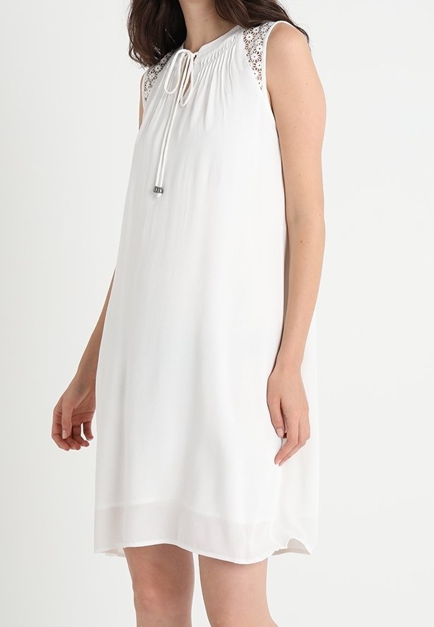 Biała bezrękawnikowa sukienka z zebranym dekoltem, dekoracyjnym koronkowym wykończeniem na ramionach oraz wiązaniem z przodu. Gładki, lekki materiał.