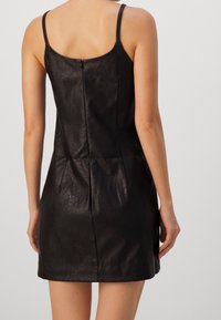 Schwarzes Leder-Minikleid mit dünnen Trägern, figurbetonter Silhouette und verdecktem Reißverschluss im Rücken. Sanfte Textur mit subtiler glänzender Optik.