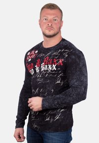 Schwarzes Langarmshirt mit strukturierter Oberfläche, mit weißen und roten grafischen Text- und Schriftsatzdesigns auf der Vorderseite.