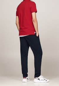 Rode polo, marineblauwe broek en witte sneakers. De polo heeft een klassieke kraag en de broek heeft een rechte pijp.