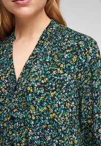 Blommig blus med svart bakgrund, med små gula, blå och rosa blommor. Knäppning fram, v-ringning och mjukt tyg.