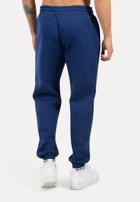 Pantaloni della tuta blu navy con vita e polsini elasticizzati, realizzati in materiale morbido. Indossati con sneakers bianche con dettaglio del logo.