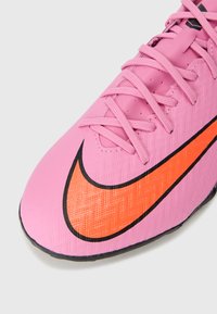 Scarpa da calcio Nike con tomaia sintetica rosa, finitura texturizzata e design Swoosh nero-arancione. Presenta lacci sottili e punta arrotondata.