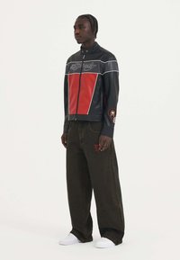 Sort læderjakke med røde paneler, hvide accenter og grafiske detaljer. Kombineret med bredskårede mørkebrune jeans og hvide sneakers.