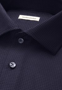 Chemise habillée bleu foncé texturée avec des boutons noirs et une étiquette blanche portant la mention "seidensticker" à l'intérieur du col.