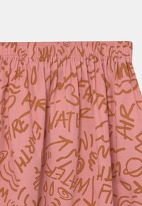 Rosa tyg med en gatherad midjeband som har bruna grafiska mönster, inklusive ord som "VATTEN" och "ELD" i olika stilar och storlekar.