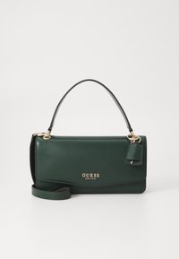 Green faux leather handbag with a short handle, gold brand logo, a detachable tag, and an optional crossbody strap. Smooth texture.