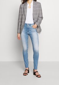 Blazer de cuadros gris sobre una blusa blanca, combinado con unos pantalones skinny azul claro y sandalias de tacón negras. Incluye hombros estructurados y un ajuste entallado.