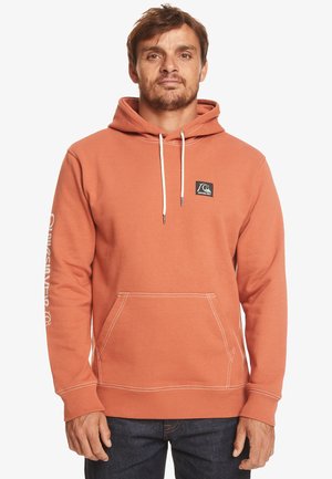 Orange hoodie med framficka, vita snören och en logotypapplikation. Har kontrasterande sömmar och text på ärmen.