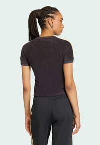 Čierny top s krátkym rukávom z textúrovaného materiálu, s raglánovými rukávmi a priliehavým strihom, v kombinácii s čiernymi nohavicami so zlatými bočnými pruhmi.