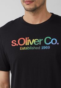 Schwarzes Baumwoll-T-Shirt mit einem Regenbogengradienten-Logo und dem Text "s.Oliver Co." sowie "Gegründet 1969" in einer lässigen Schriftart. Einfach und mit kurzen Ärmeln.