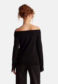 Černý svetr s odhalenými rameny a dlouhými rukávy, s žebrovaným výstřihem a manžetami, s postranními rozparky na lemu, hladká textura.