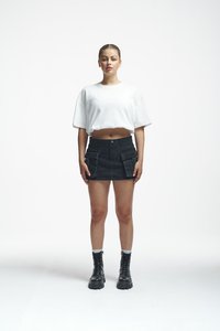 Camiseta blanca corta, minifalda de mezclilla negra con bolsillos frontales y botas negras con cordones y suelas rugosas; la modelo está de pie frente a la cámara.