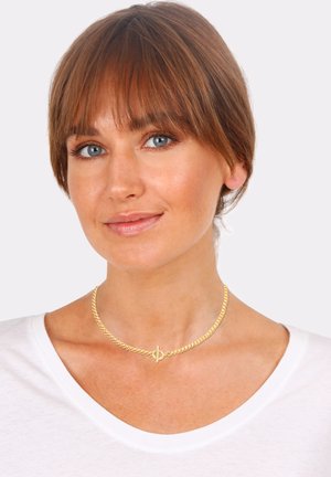 Gold-tone choker necklace with a twisted chain design and a circular clasp, worn on a bare neck. Background is plain white.