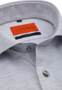 Hellgraues Slim-Fit-Hemd mit glatter Textur, ausgestattet mit einem Button-Down-Kragen, einem orangen Plakettenetikett und einer einzelnen grauen Knopfdetails.