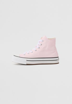 Różowy wysokotonowy tenisówka z płótna z białymi sznurowadłami, grubą białą podeszwą z dwoma czarnymi paskami, widok z boku na jednolitym tle.