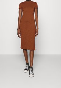 Ruskea, lyhythihainen, vartalonmyötäinen midi-mekko, joka on valmistettu tekstuuri-kankaasta ja yhdistetty mustiin korkeatoppaisiin tennareihin. Yksinkertainen muotoilu, kapea istuvuus.