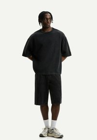 Oversized black cotton T-shirt and matching black denim shorts. Model wears cream sneakers with textured accents and white socks.