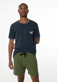 T-shirt bleu marine à manches courtes avec des finitions blanches et une poche portant le logo "NXG", associé à un short vert olive avec cordon de serrage à la taille et poches latérales.