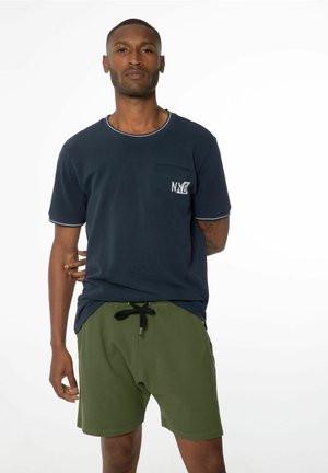Marineblaues Kurzarm-T-Shirt mit weißen Nähten und Tasche, auf der das "NXG"-Logo prangt, kombiniert mit olivgrünen Shorts, mit Kordelzugbund und Seitentaschen.