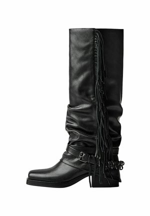 Black leather knee-high boots with slouchy design, side fringe details, a buckled strap, and a slightly curved block heel.