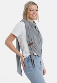 Grijze gebreide sjaal met een textuurpatroon, voorzien van een bruine leren accent en verstelbare banden voor styling. Draag over een wit shirt.