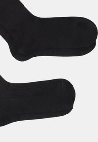 Un paio di calzini neri semplici a collo, disposti in piano, che mostrano le zone del tallone e delle punte, su uno sfondo grigio chiaro.