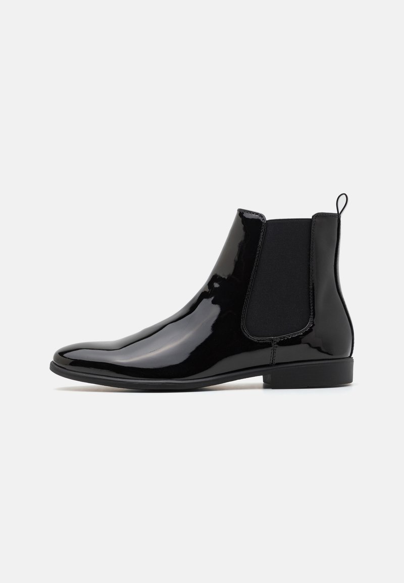 Bottines Chelsea en cuir verni noir avec des panneaux latéraux élastiques et une languette, présentant un profil slim et une semelle en caoutchouc plate.