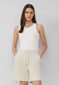 Weißes rippenförmiges Tanktop, kombiniert mit hellbeigen Shorts mit elastischem Bund und seitlichen Taschen, durchgehend mit weicher Textur.