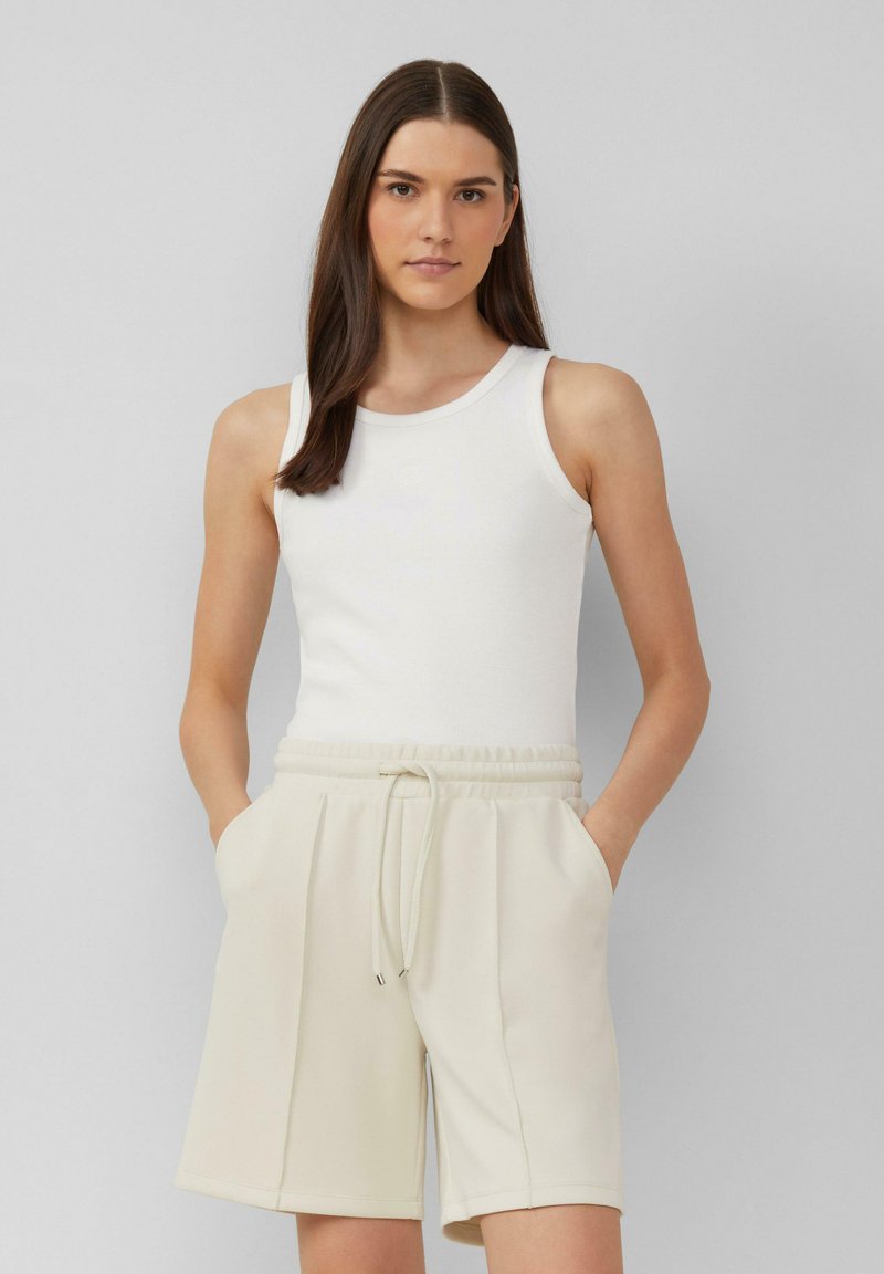 Weißes rippenförmiges Tanktop, kombiniert mit hellbeigen Shorts mit elastischem Bund und seitlichen Taschen, durchgehend mit weicher Textur.