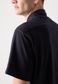 Polo shirt navy in un tessuto morbido, con maniche corte e colletto. Presenta un motivo sottile e cuciture delle spalle rinforzate.