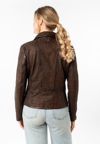 Chaqueta de cuero marrón con un patrón de estampado de leopardo, diseño ajustado y detalles de costura. Combinada con unos jeans de color azul claro.