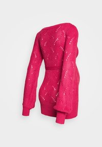 Stickad tröja i klar rosa med långa ärmar. Har ett texturerat kabelemönster och ett bälte i midjan, som slutar vid den nedre höften.