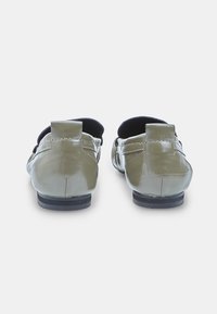 Mocassins vert olive avec une finition brillante, présentant un petit talon, un design à enfiler et des détails cousus le long des côtés et à l'arrière.