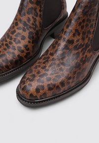 Botas de tobillo con estampado de leopardo marrón, textura brillante, paneles laterales elásticos y un tacón bajo apilado. Adecuadas para un uso casual.