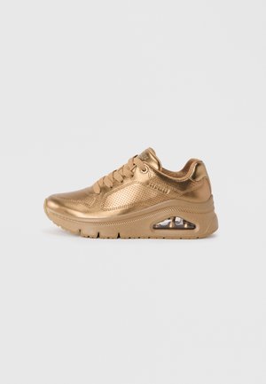 Gold metallic sneaker with a smooth texture, featuring perforated details, lace-up design, and an air cushioning visible in the sole.
